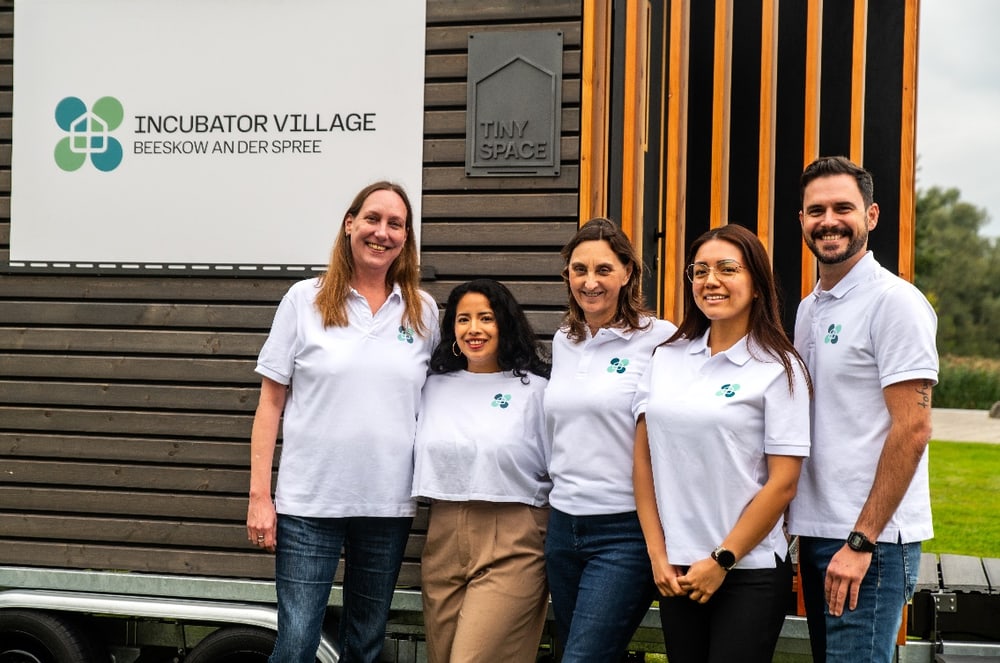 Das Team des Incubator Village Beeskow steht vor einem Tiny Space – Sonja Schwarzkopf und Kolleginnen und Kollegen in weißen Polo-Shirts mit dem IVB-Logo